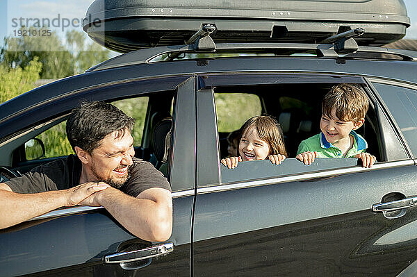 Glücklicher Vater mit Kindern  die an einem sonnigen Tag durch das Autofenster schauen