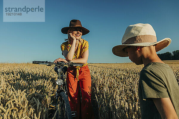 Mutter beobachtet Sohn  der neben Fahrrad im Weizenfeld steht