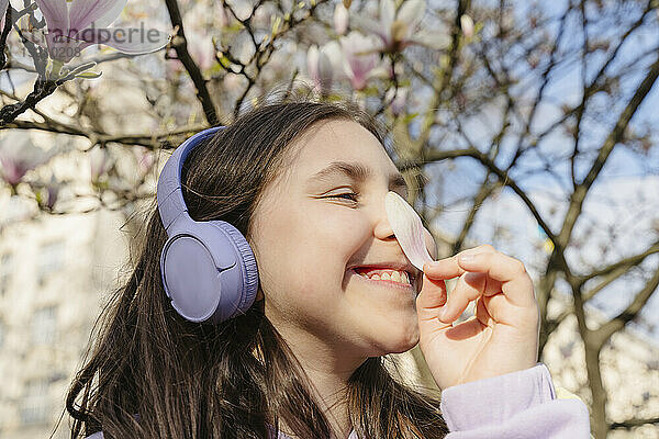 Lächelndes Mädchen riecht Blütenblatt unter Magnolienbaum