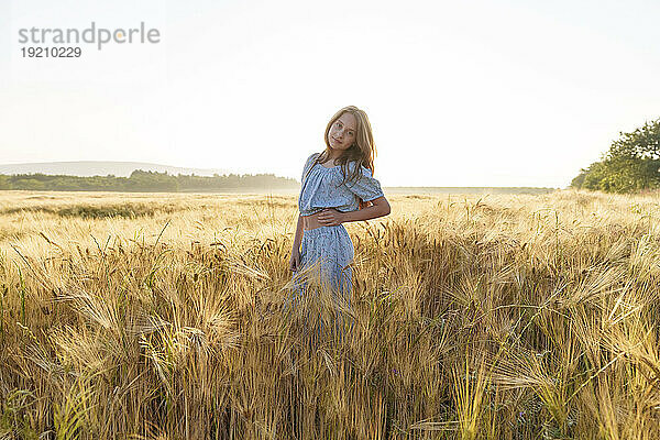 Mädchen mit der Hand auf der Hüfte steht inmitten der Weizenernte im Feld