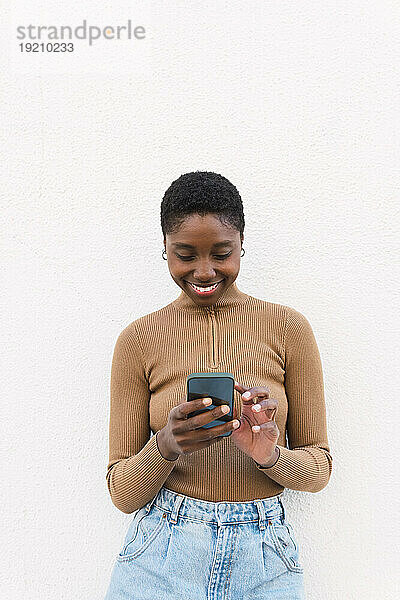 Lächelnde Frau  die ihr Mobiltelefon vor der Wand benutzt