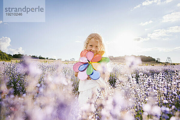 Lächelndes Mädchen hält Windradspielzeug im Lavendelfeld