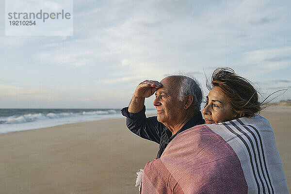 Lächelnde ältere Frau umarmt Mann  der am Strand steht