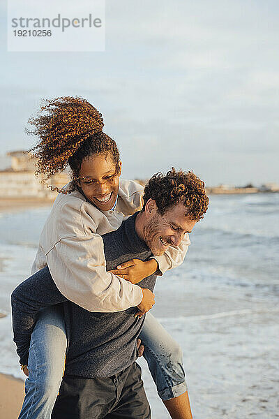 Smiling man giving piggyback ride to girlfriend at beach