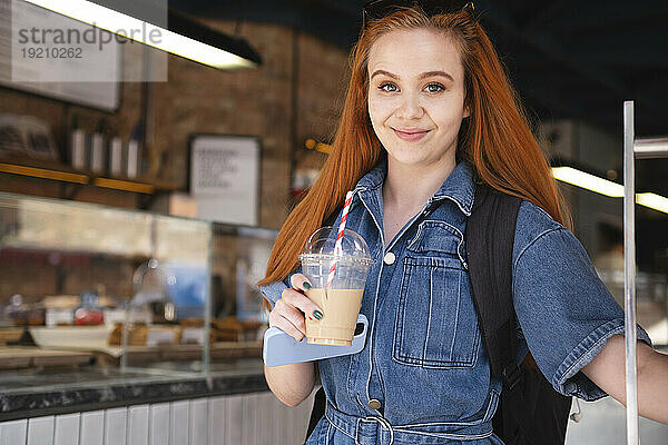 Lächelnde Geschäftsfrau hält Kaffee und Smartphone im Café