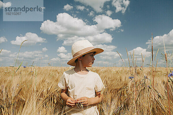 Nachdenklicher Junge steht inmitten von Weizenfeldern