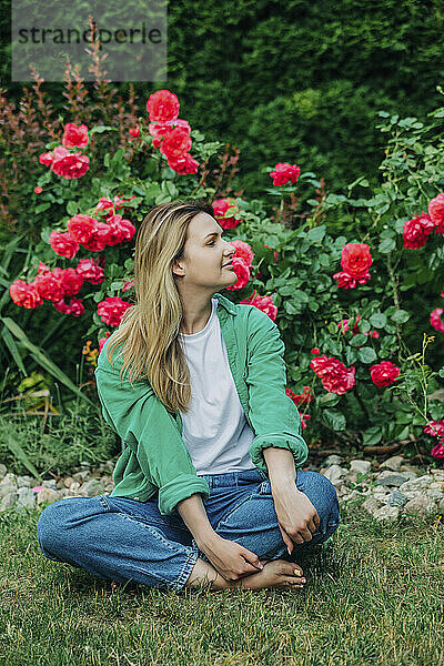 Lächelnde Frau sitzt vor Rosenpflanzen im Garten