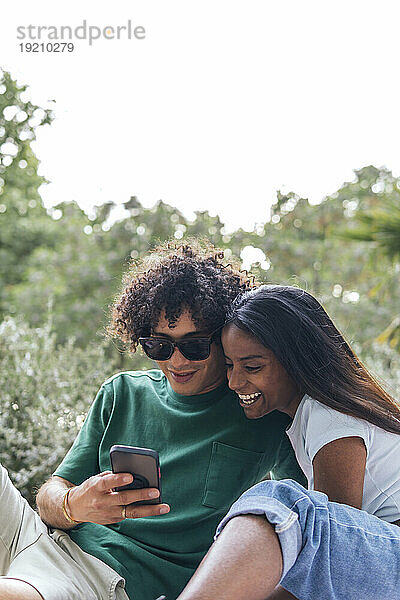 Lächelnder Freund zeigt Freundin im Park Smartphone