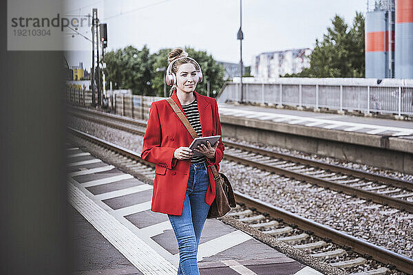 Lächelnde Frau mit Tablet-PC läuft auf Bahnsteig