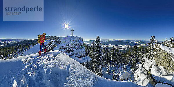 Woman in ski-wear hiking near summit cross on snowcapped mountain