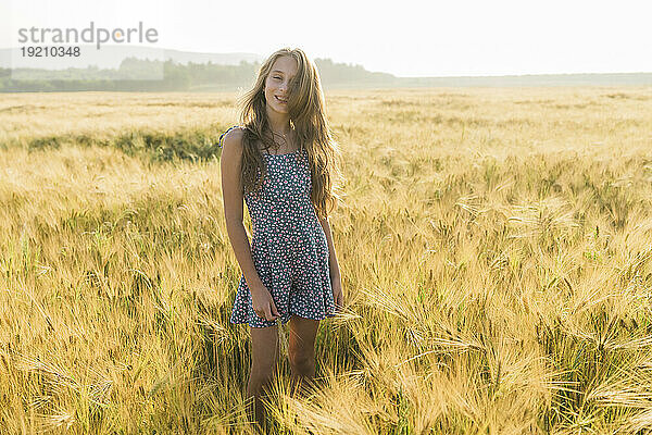 Lächelndes Mädchen  das inmitten einer Weizenernte auf dem Feld steht