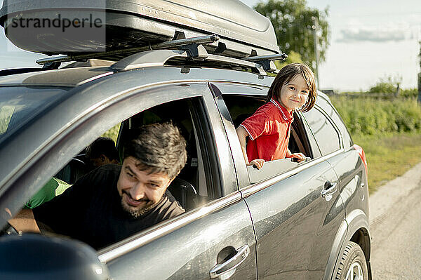 Smiling father with son leaning out of car window on sunny day