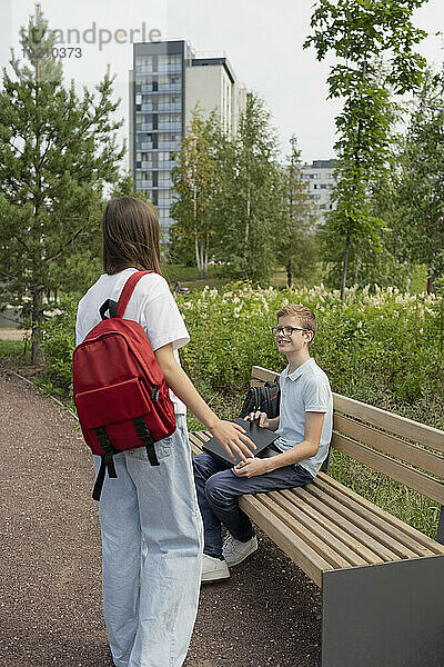 Girl talking to friend sitting on on bench at park