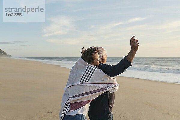 Ältere Frau umarmt Mann  der am Strand steht