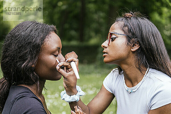 Junge Frau schminkt ihre Freundin im Park