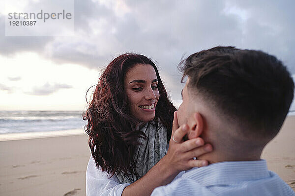 Happy woman touching boyfriend's face at beach