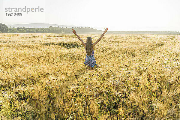 Mädchen mit ausgestreckten Armen steht inmitten der Ernte im Weizenfeld