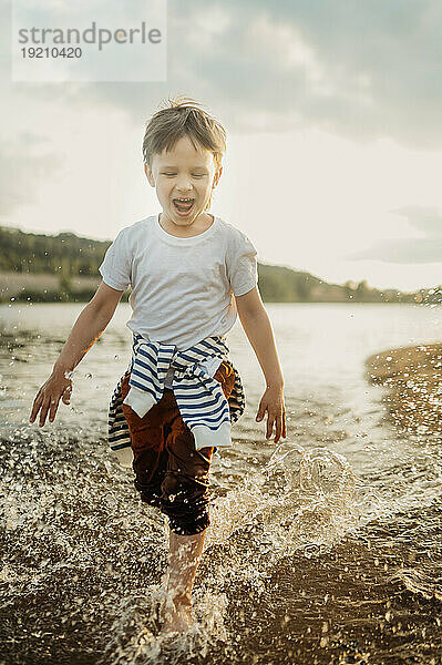 Carefree boy splashing water in sea at beach