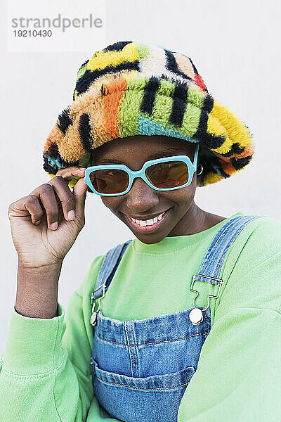 Happy young woman wearing multi colored hat and sunglasses against white background