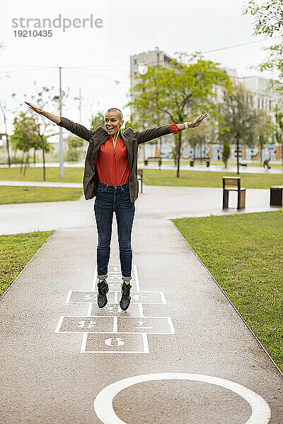 Carefree woman with arms outstretched playing hopscotch at park