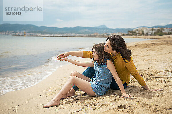 Glückliche Mutter und Tochter sitzen zusammen im Sand am Strand