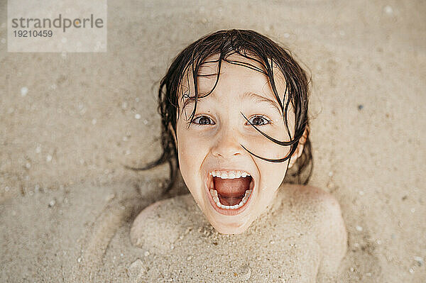 Cheerful boy covered with sand having fun at beach