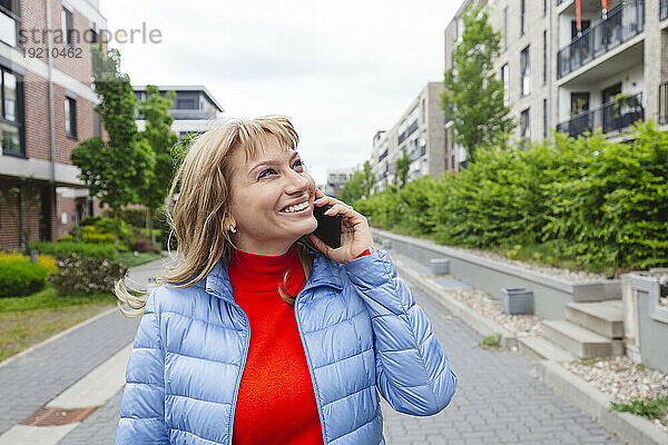 Lächelnde Frau  die in der Nähe eines Wohngebiets mit ihrem Smartphone spricht