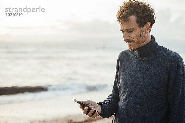 Mann benutzt Smartphone am Strand