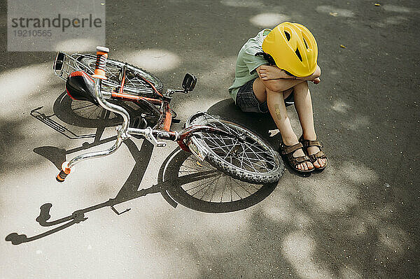 Verärgerter Junge sitzt neben Fahrrad auf Fußweg