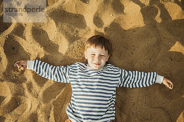 Lächelnder Junge  der auf Strandsand liegt