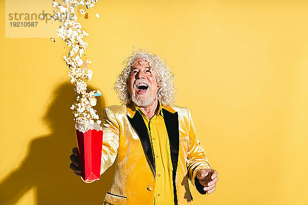 Fröhlicher älterer Mann wirft Popcorn vor gelbem Hintergrund