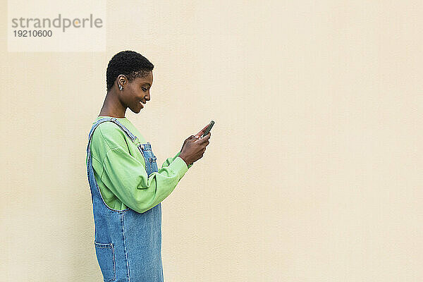 Glückliche junge Frau benutzt Smartphone vor beigefarbener Wand