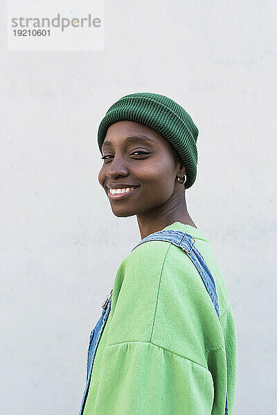 Happy woman wearing green knit hat in front of white wall