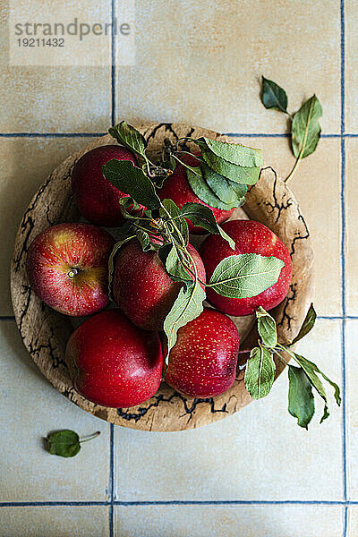 Holzschale mit roten Äpfeln auf gefliestem Küchentisch