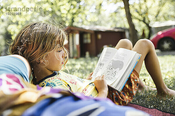 Blonder Junge liest Buch und liegt neben seiner Mutter im Wald