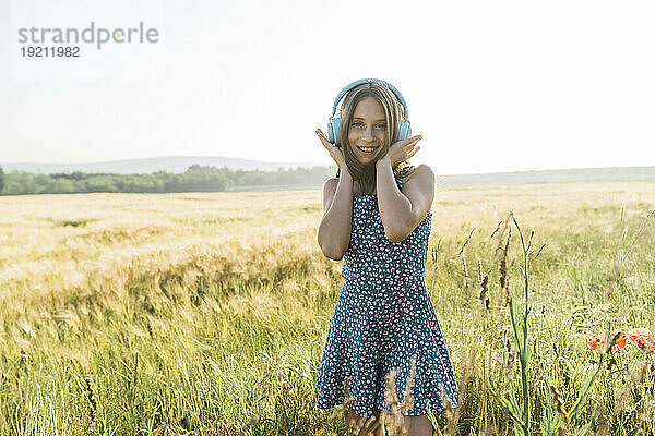 Fröhliches Mädchen  das mit kabellosen Kopfhörern im Mohnfeld Musik hört