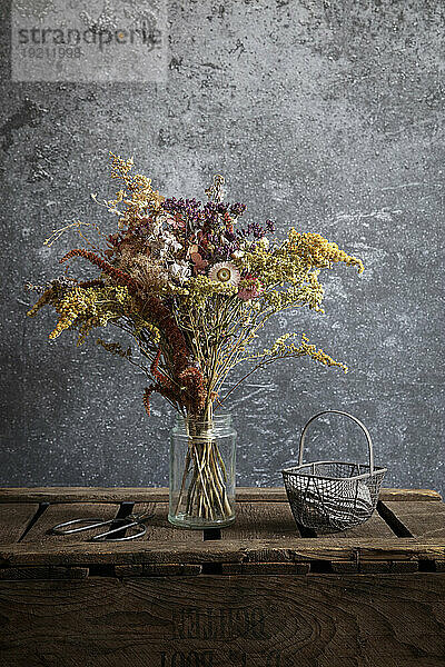Arrangement of dried flowers in jar standing on wooden crate