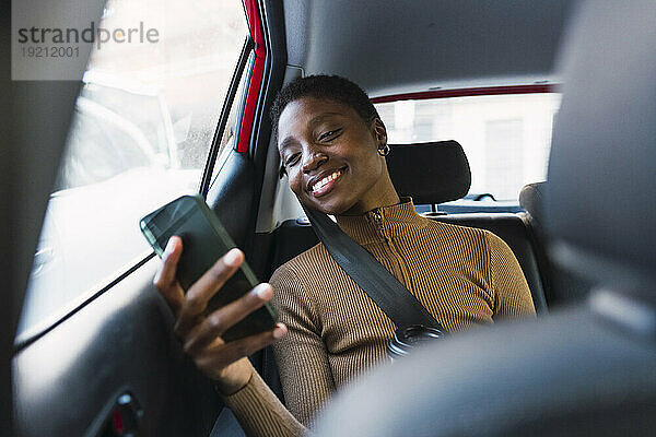 Glückliche junge Frau benutzt Smartphone im Auto