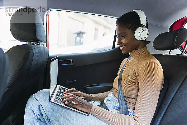 Glückliche junge Frau mit kabellosen Kopfhörern sitzt im Auto
