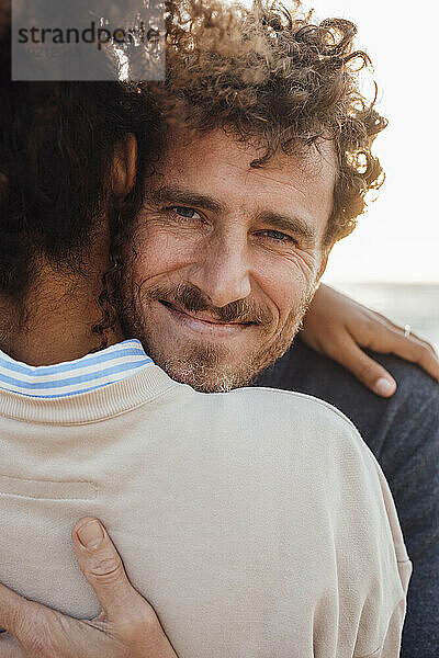 Lächelnder Mann umarmt Freundin am Strand