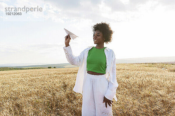Smiling woman holding paper plane standing in field