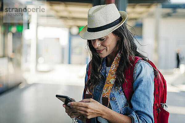 Glückliche Frau benutzt Smartphone an der Straßenbahnhaltestelle