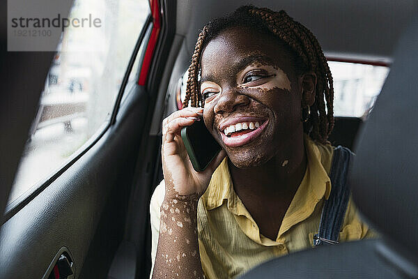 Glückliche junge Frau  die im Auto mit dem Smartphone spricht