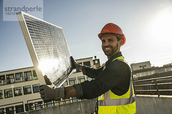 Ingenieur trägt Schutzkleidung und hält an einem sonnigen Tag ein Solarpanel