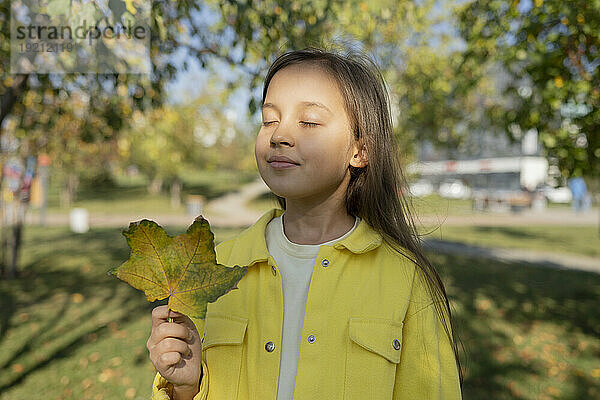 Mädchen mit geschlossenen Augen hält Ahornblatt im Park