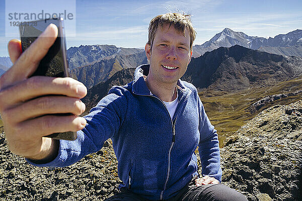 Glücklicher Mann  der an einem sonnigen Tag ein Selfie in der Nähe des Berges macht