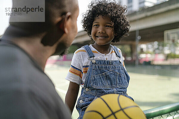 Glücklicher Sohn im Gespräch mit Vater auf dem Basketballplatz