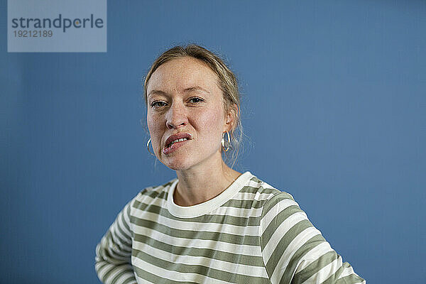 Frau beißt sich auf die Lippe vor blauem Hintergrund