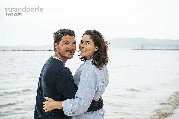 Glücklicher Mann und Frau stehen zusammen vor dem Meer am Strand