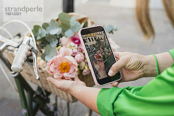 Frau fotografiert Blumen im Fahrradkorb per Smartphone